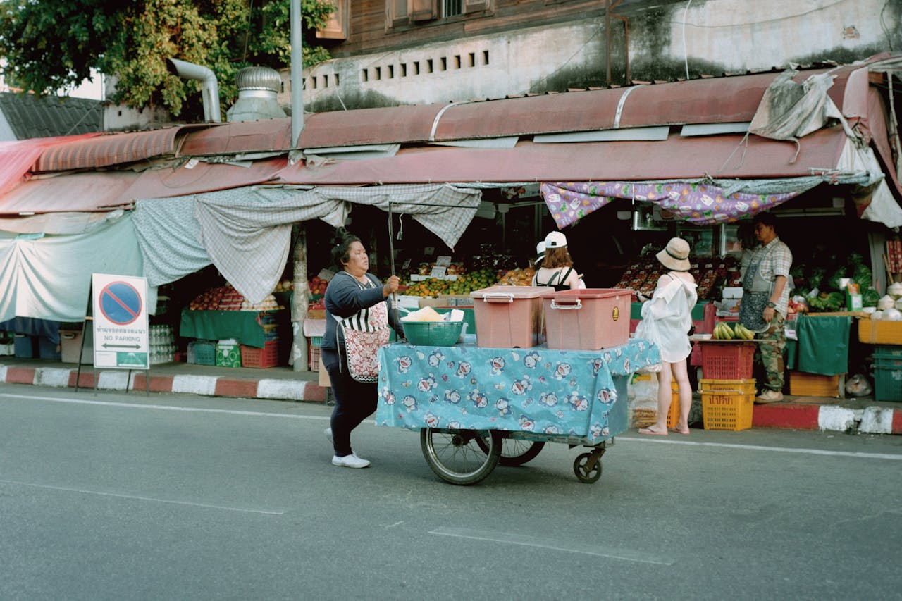 gallery-1 A bustling urban street market with a vendor pushing a cart, surrounded by market stalls and pedestrians.