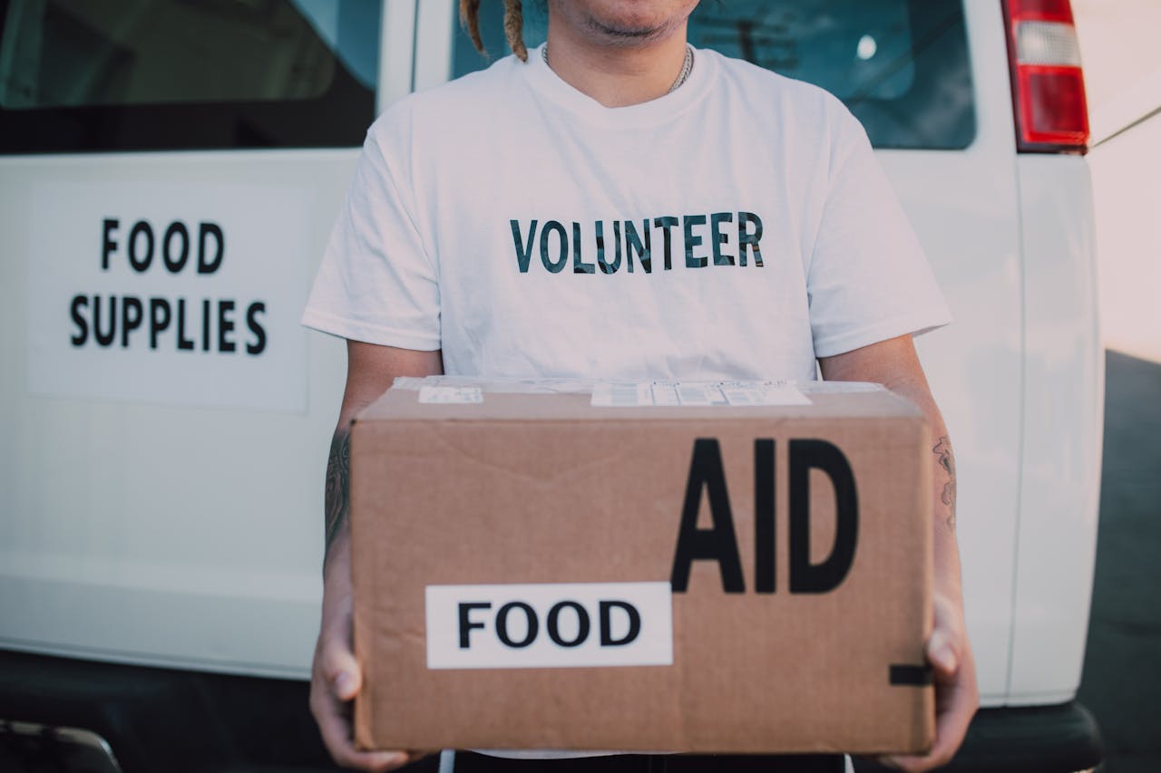 about-01 A volunteer holding a food aid box in front of a supply vehicle, ready for distribution.