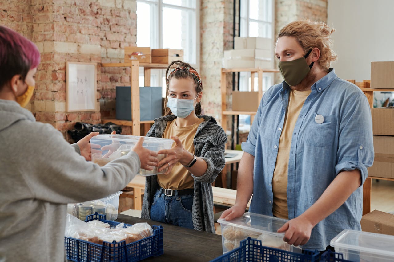 hero-img-01 Volunteers wearing masks distribute food in a donation center, focusing on charity and community support.